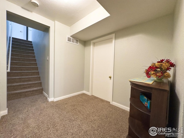 below grade area featuring visible vents, baseboards, stairs, a textured ceiling, and carpet floors