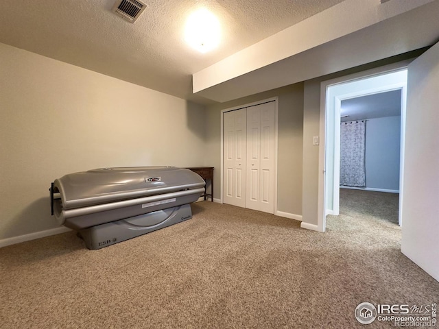 interior space featuring a textured ceiling, carpet, visible vents, and baseboards