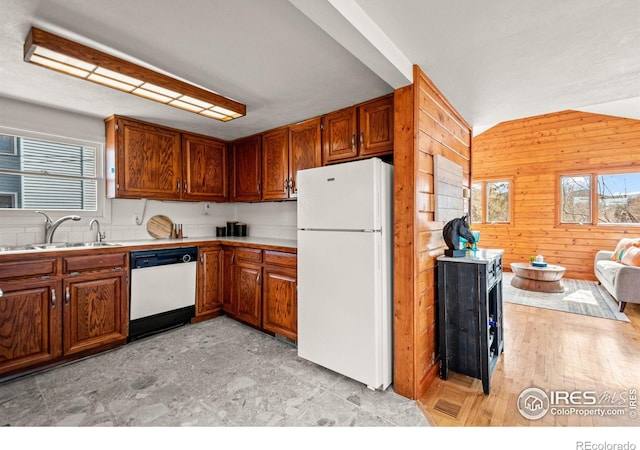 kitchen with white appliances, brown cabinetry, light countertops, wood walls, and a sink