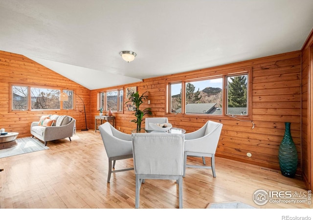 dining space featuring lofted ceiling, wood walls, and light wood-style flooring