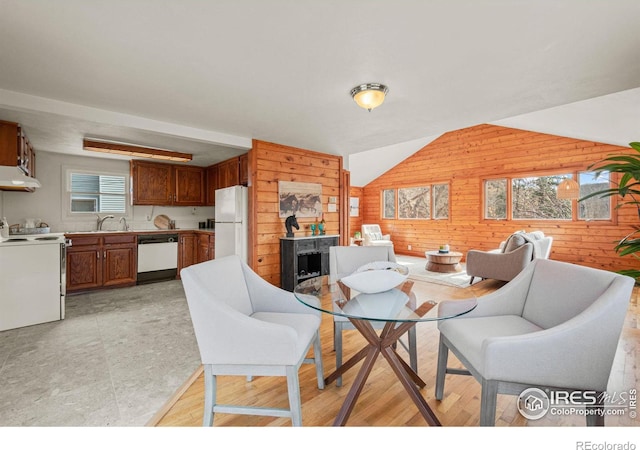 dining space featuring lofted ceiling, wood walls, light wood-type flooring, and a wealth of natural light