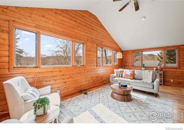 living room with lofted ceiling, ceiling fan, wood walls, and wood finished floors