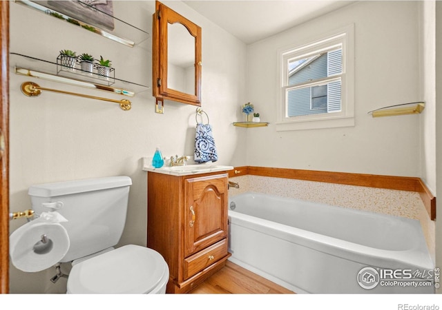 bathroom featuring toilet, vanity, a bath, and wood finished floors