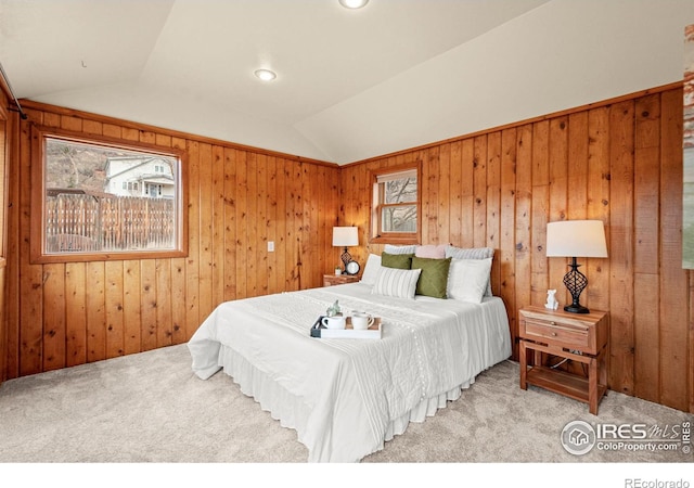 carpeted bedroom with vaulted ceiling, multiple windows, and wooden walls