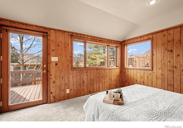 carpeted bedroom with access to outside, vaulted ceiling, and wood walls