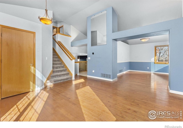 unfurnished living room with baseboards, visible vents, stairway, wood finished floors, and high vaulted ceiling