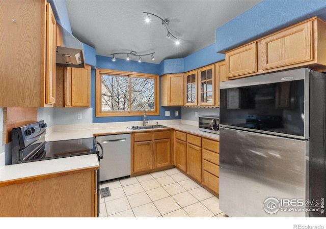 kitchen with light tile patterned floors, glass insert cabinets, stainless steel appliances, light countertops, and a sink