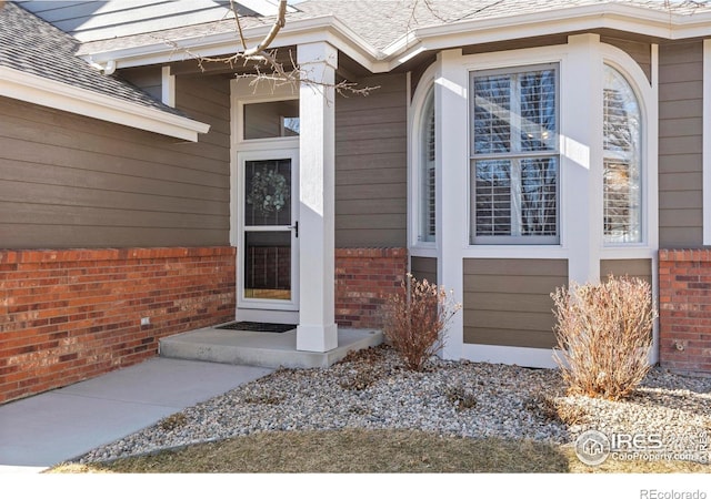 property entrance featuring a shingled roof and brick siding