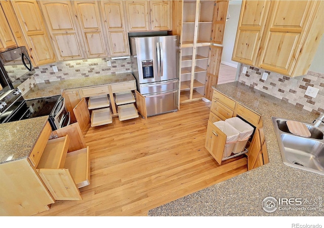 kitchen with light wood-style flooring, stainless steel appliances, a sink, light brown cabinetry, and tasteful backsplash