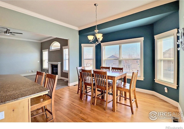 dining room with ornamental molding, light wood finished floors, a glass covered fireplace, and baseboards