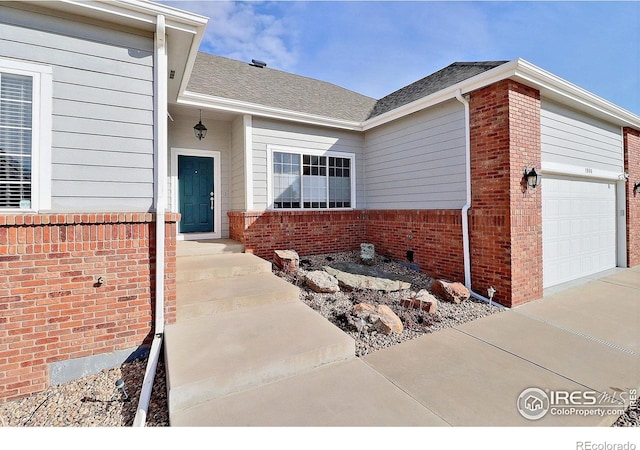 view of exterior entry featuring an attached garage, brick siding, and a shingled roof