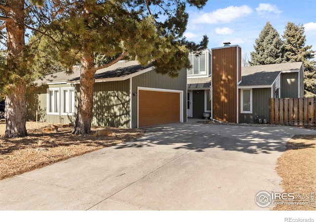 view of front of property featuring a garage, a shingled roof, fence, concrete driveway, and a chimney