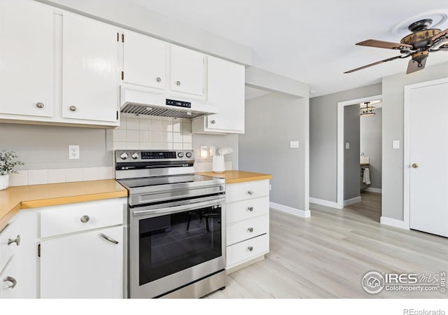 kitchen featuring under cabinet range hood, light countertops, light wood-type flooring, backsplash, and stainless steel range with electric stovetop