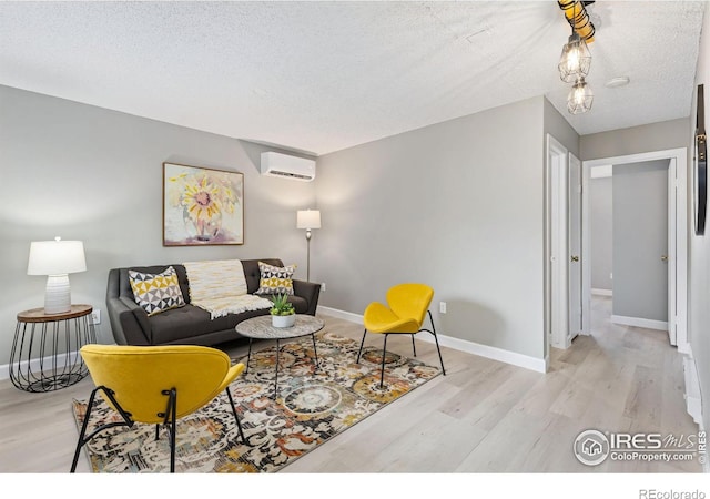 living area featuring a wall unit AC, a textured ceiling, baseboards, and wood finished floors