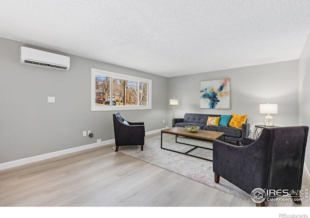 living area with wood finished floors, a textured ceiling, baseboards, and a wall mounted AC