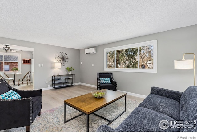 living room featuring light wood-style flooring, baseboards, a textured ceiling, and a wall mounted air conditioner