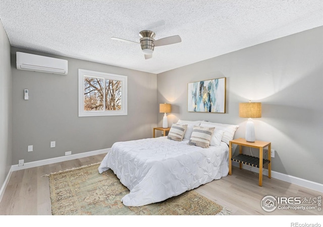 bedroom featuring a textured ceiling, an AC wall unit, wood finished floors, and baseboards