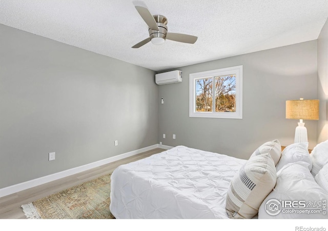 bedroom with baseboards, a ceiling fan, wood finished floors, a textured ceiling, and an AC wall unit