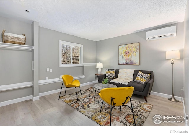 living area with a wall unit AC, a textured ceiling, baseboards, and wood finished floors