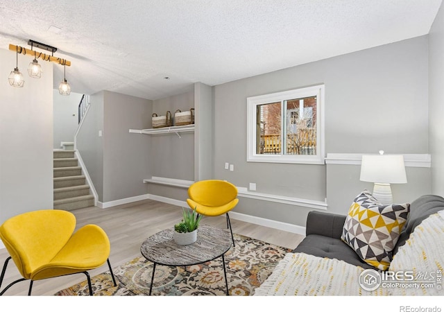 living area featuring baseboards, stairway, a textured ceiling, and wood finished floors