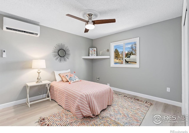 bedroom featuring a textured ceiling, a wall mounted AC, baseboards, and light wood-style floors