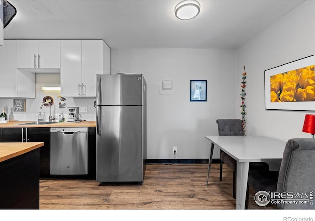 kitchen featuring butcher block counters, wood finished floors, stainless steel appliances, white cabinetry, and a sink