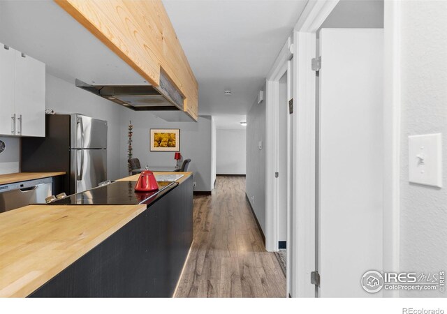 kitchen with wood finished floors, baseboards, white cabinets, wooden counters, and appliances with stainless steel finishes