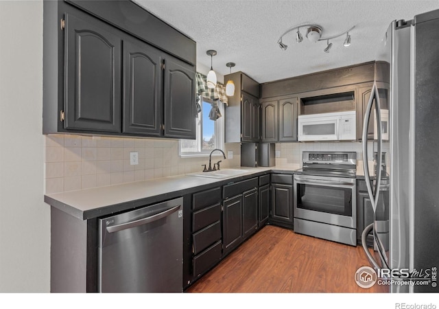 kitchen featuring backsplash, appliances with stainless steel finishes, a sink, a textured ceiling, and wood finished floors