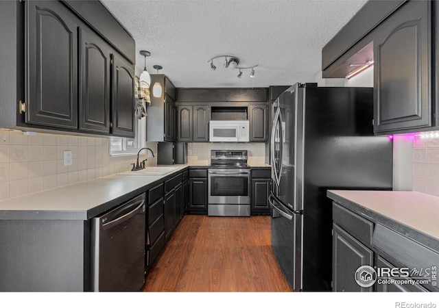 kitchen with dark wood-style flooring, decorative backsplash, appliances with stainless steel finishes, a sink, and a textured ceiling