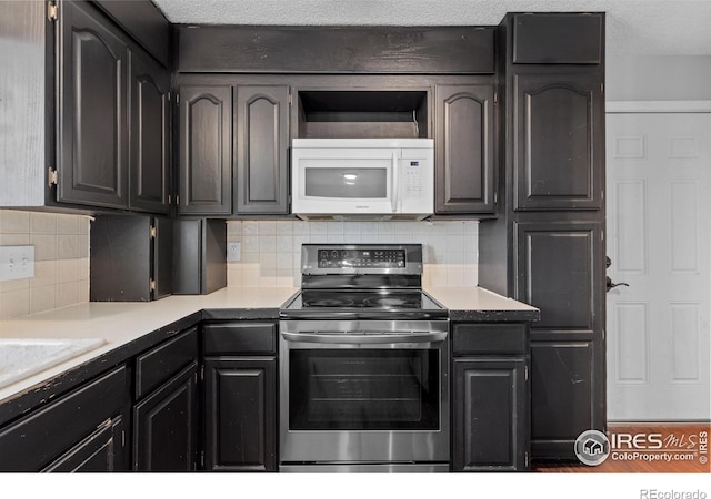 kitchen featuring decorative backsplash, white microwave, stainless steel electric stove, light countertops, and a textured ceiling