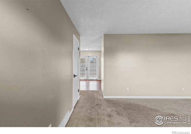 unfurnished room with a textured ceiling, carpet flooring, and baseboards