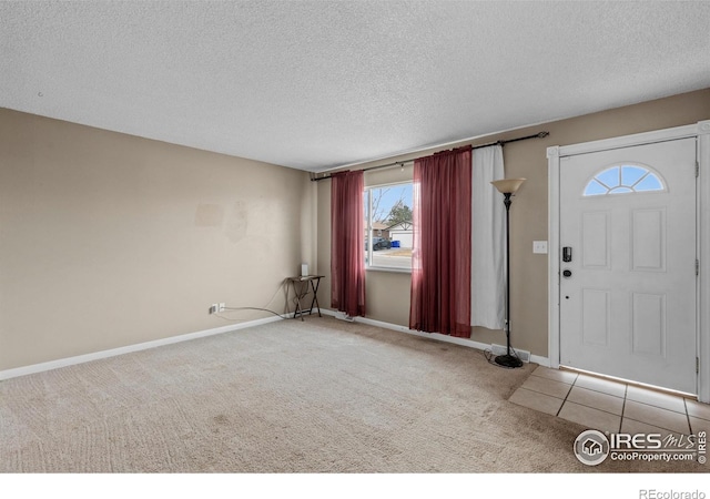 carpeted entrance foyer featuring tile patterned flooring, a textured ceiling, and baseboards