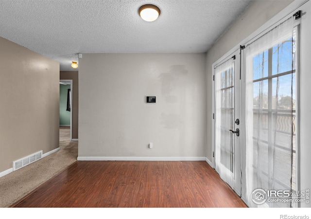 foyer entrance with french doors, visible vents, a textured ceiling, wood finished floors, and baseboards