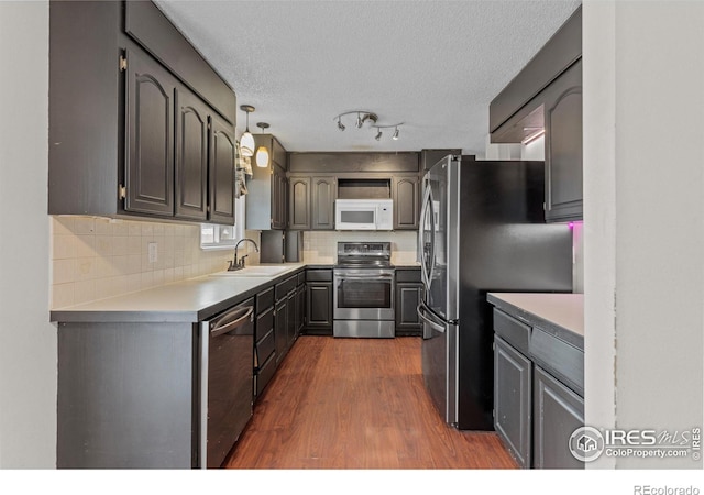 kitchen with dark wood-style flooring, stainless steel appliances, tasteful backsplash, light countertops, and a sink