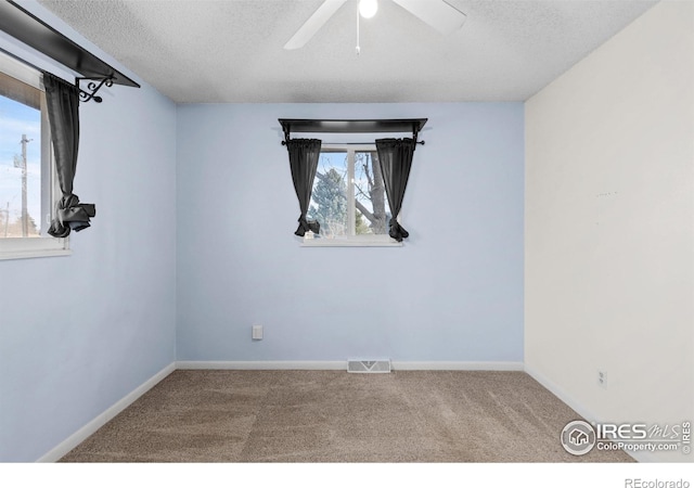 carpeted empty room featuring a textured ceiling, a ceiling fan, visible vents, and baseboards