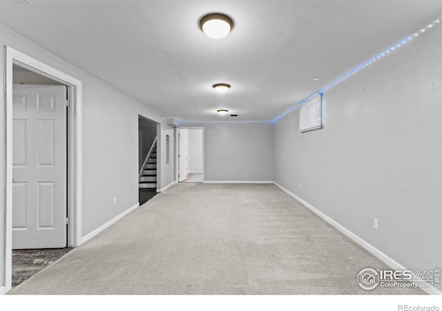 finished basement with stairs, carpet floors, a textured ceiling, and baseboards