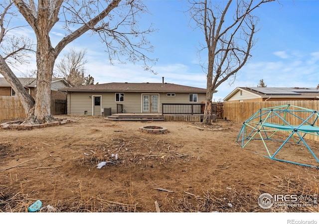 rear view of property with an outdoor fire pit, a wooden deck, a fenced backyard, and french doors