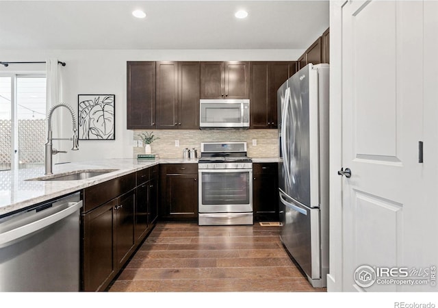 kitchen with light stone counters, a sink, dark brown cabinets, appliances with stainless steel finishes, and backsplash