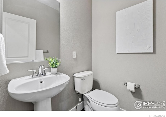 bathroom with toilet, a sink, and a textured wall