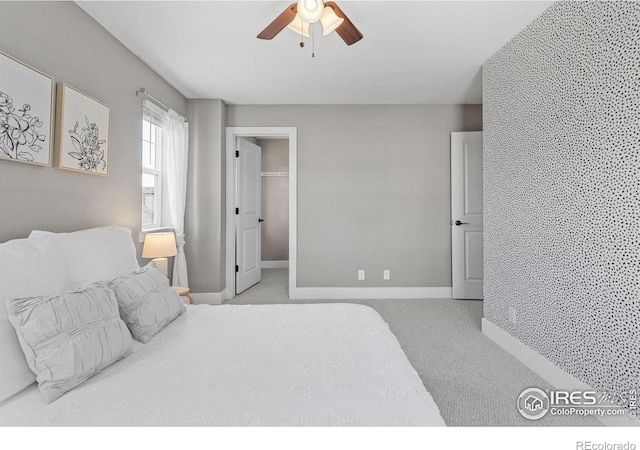 carpeted bedroom with ceiling fan, a spacious closet, and baseboards