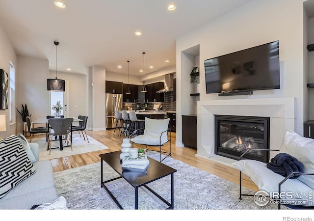 living room with light wood finished floors, a glass covered fireplace, and recessed lighting