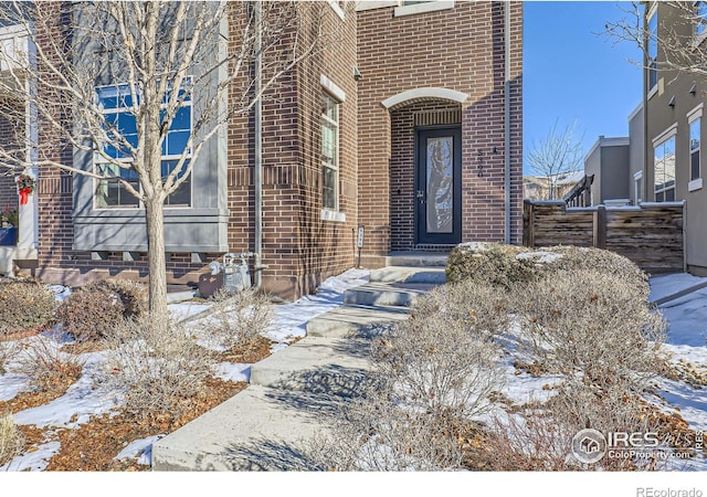 snow covered property entrance with brick siding