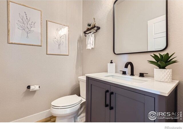 half bath featuring toilet, baseboards, wood finished floors, and vanity