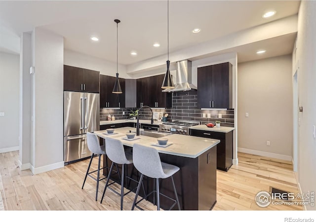 kitchen featuring light wood finished floors, an island with sink, a breakfast bar area, wall chimney range hood, and high end fridge