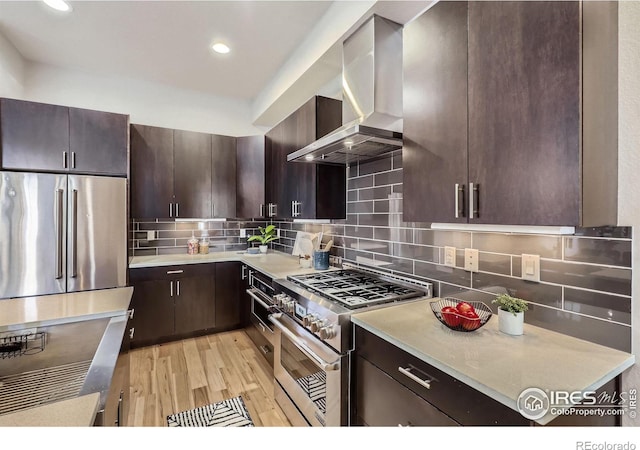 kitchen with high quality appliances, light countertops, dark brown cabinets, wall chimney range hood, and backsplash