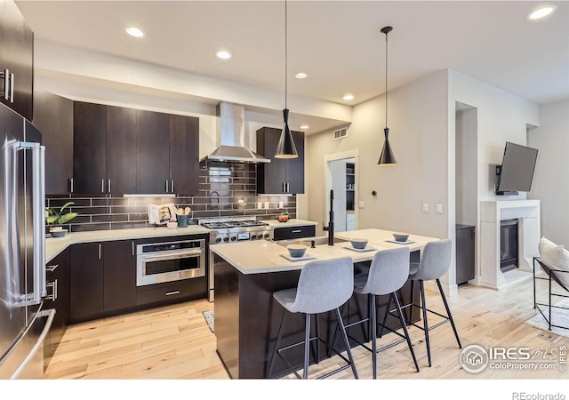 kitchen with premium appliances, visible vents, light countertops, wall chimney exhaust hood, and a kitchen bar