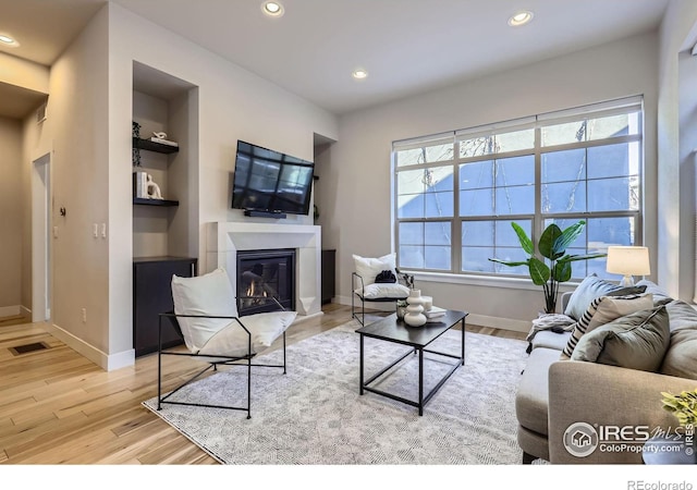 living area with built in shelves, recessed lighting, a glass covered fireplace, wood finished floors, and baseboards