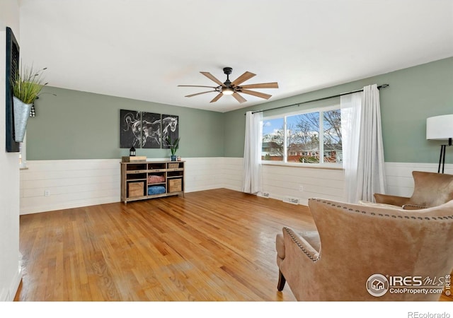 unfurnished room featuring a ceiling fan, a wainscoted wall, visible vents, and wood finished floors