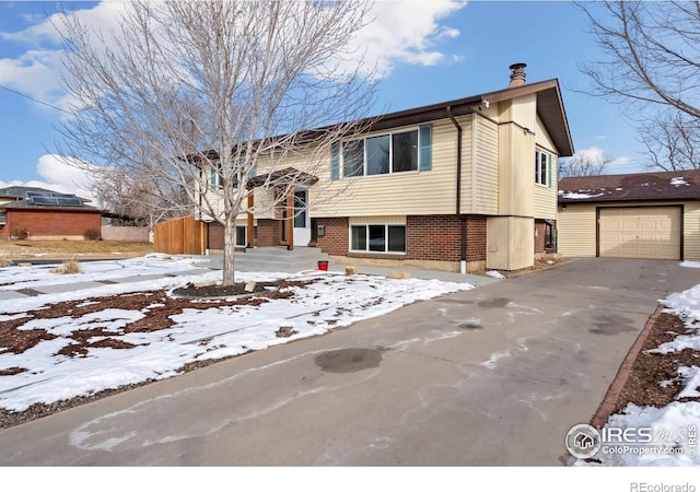 split foyer home featuring brick siding, driveway, a chimney, and a detached garage