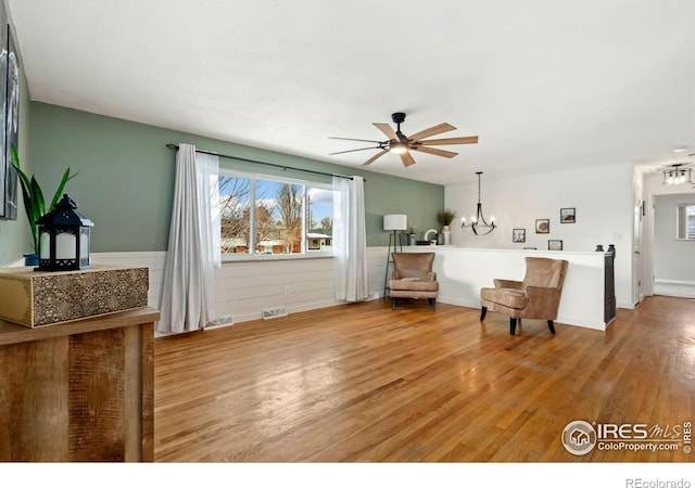 interior space with light wood-style floors, wainscoting, visible vents, and ceiling fan with notable chandelier